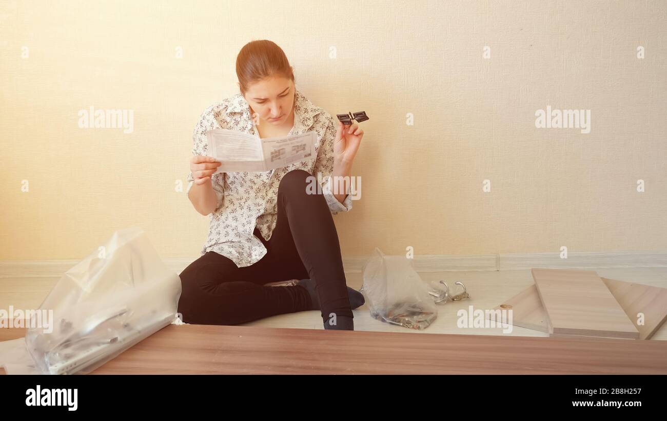 serious housewife sits on floor and reads directive looking at cabinet furniture fasteners in apartment kitchen copy space Stock Photo