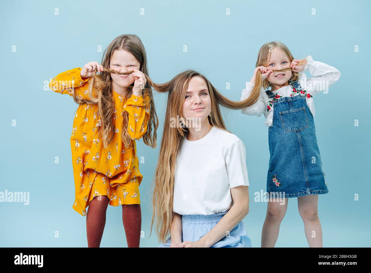 Daughters playing with their mother's hair making hair mustache over blue Stock Photo
