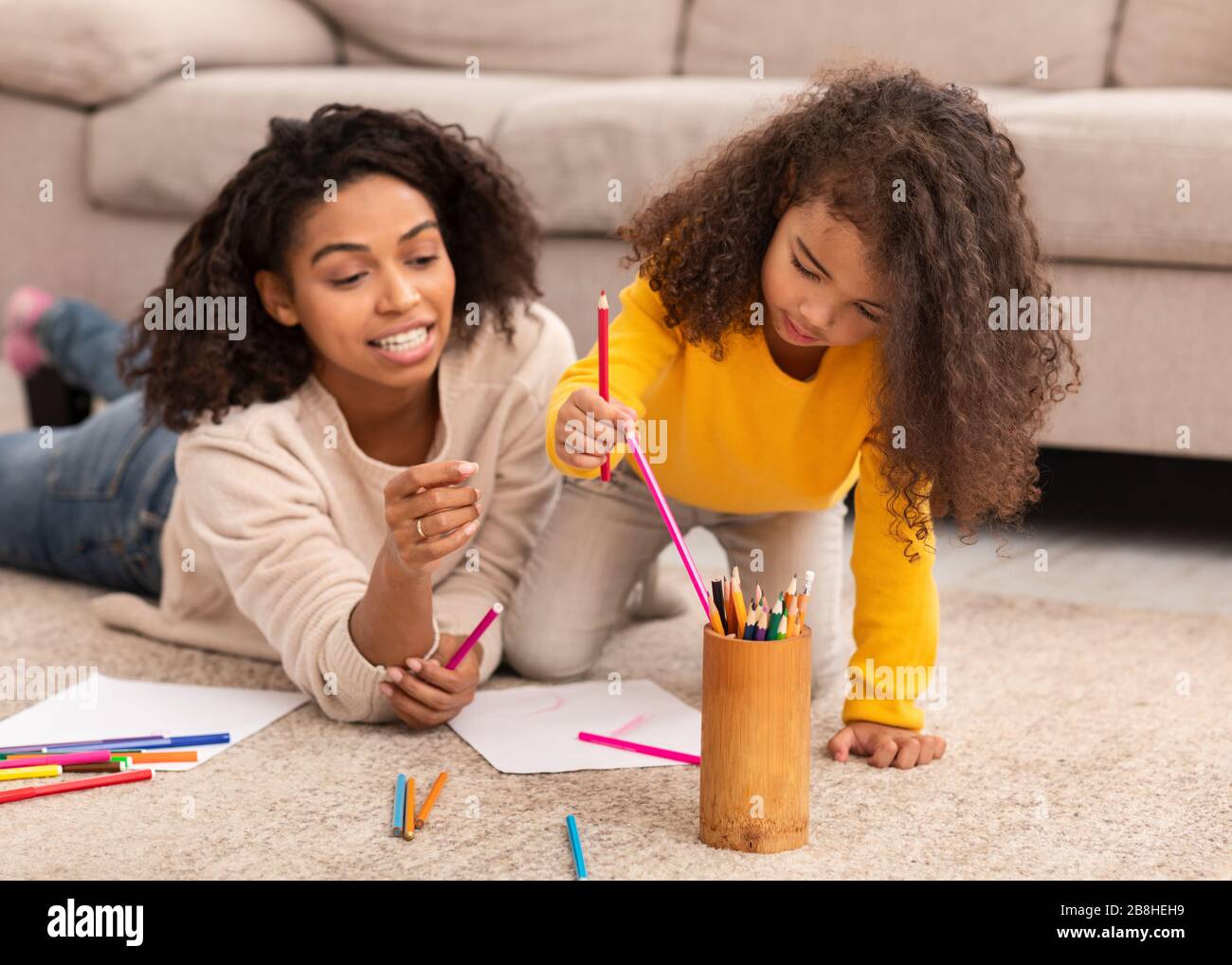 Black Mother And Little Daughter Sketching Lying On Floor Indoors Stock Photo