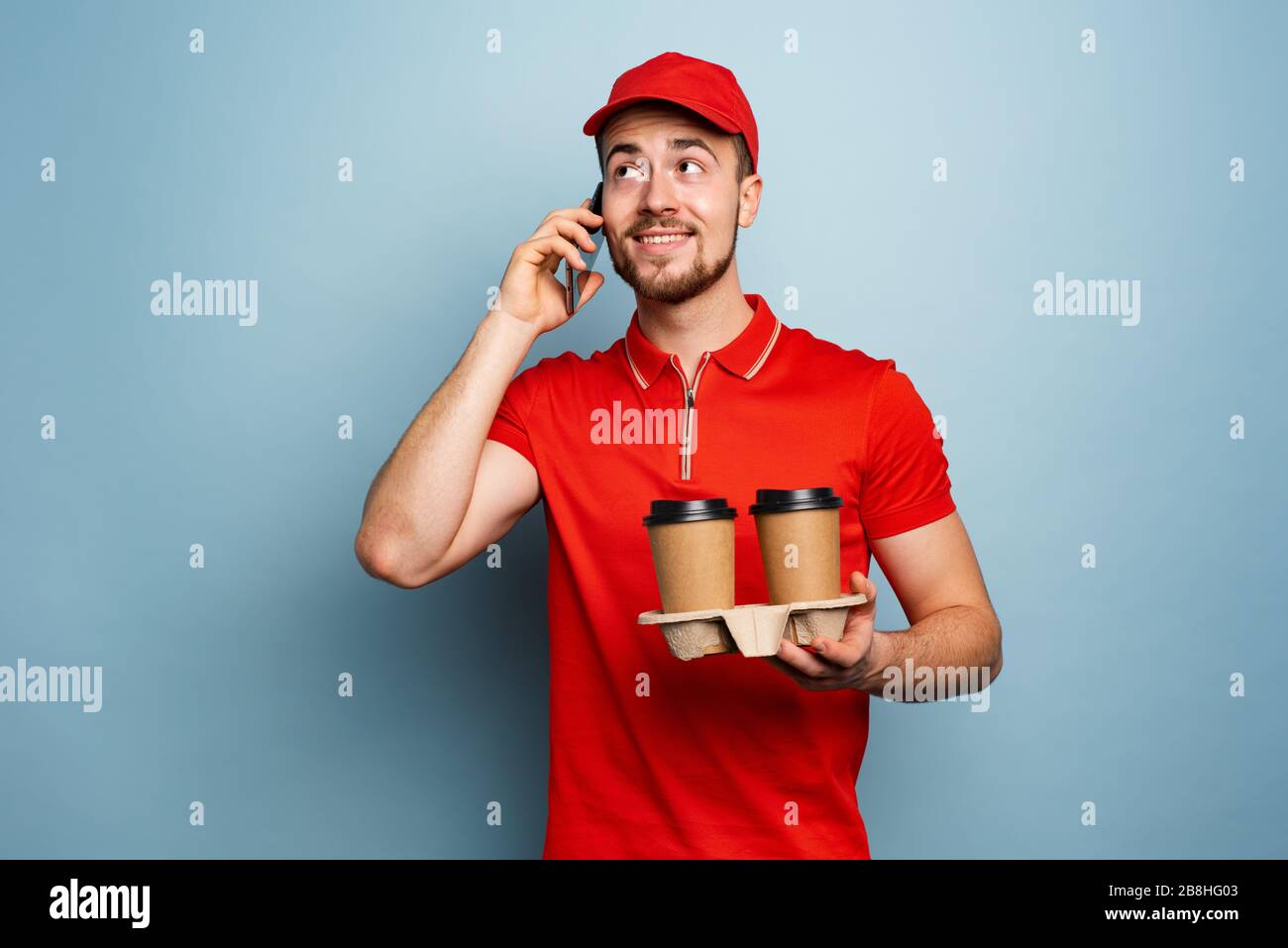 Courier delivers hot coffee and receive call on phone. Cyan background Stock Photo
