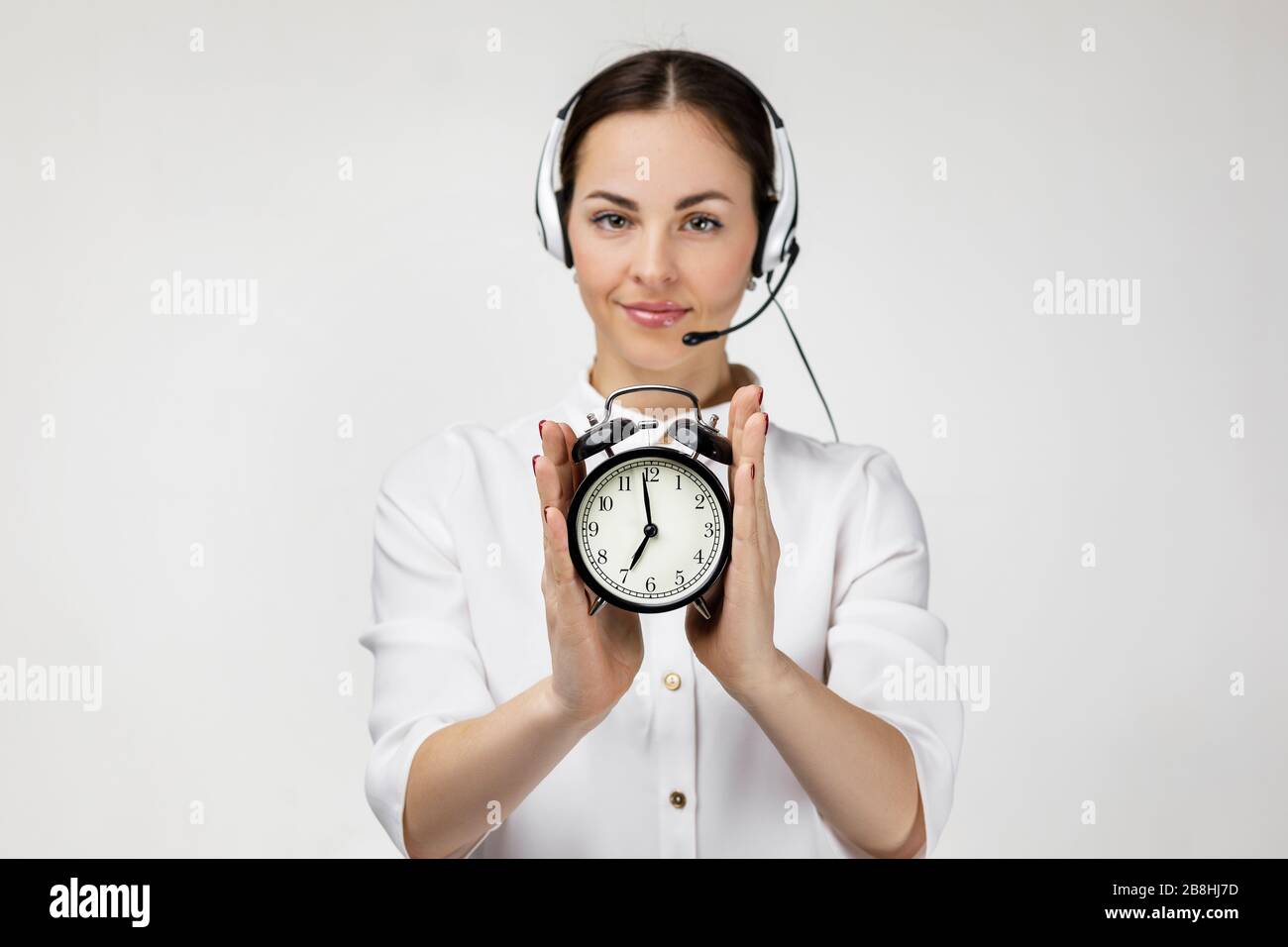 Beautiful smiling woman consultant of call center in headphones holding  alarm clock on gray background. female customer support operator with  headset. save your time Stock Photo - Alamy