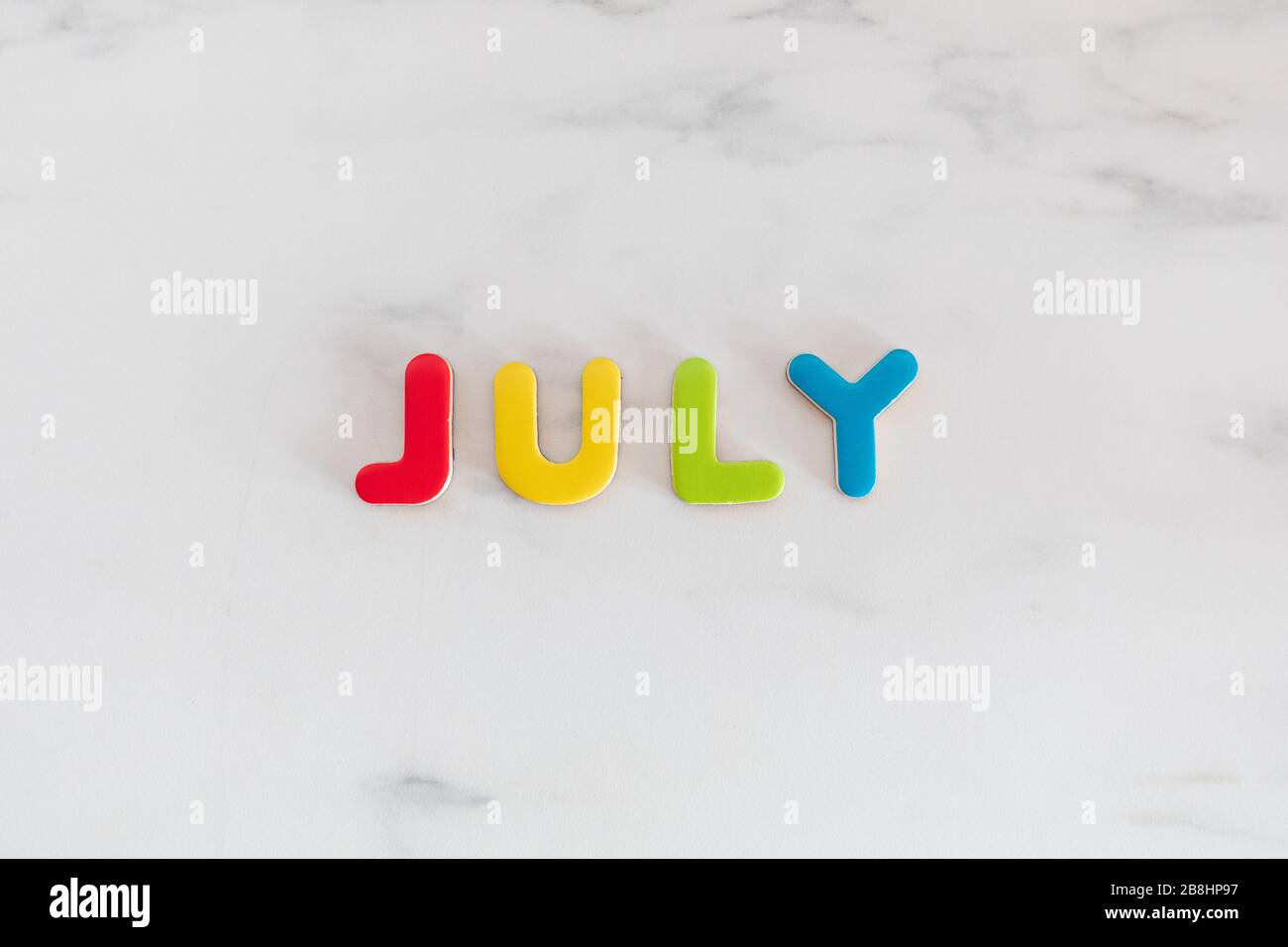 July word written with colorful letters on white marble stone background, top view Stock Photo