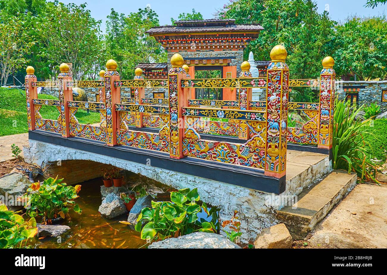The richly decorated carved wooden bridge with floral and animalistic elements, traditional Thai and Bhutanese flowers of golden shower and blue poppy Stock Photo
