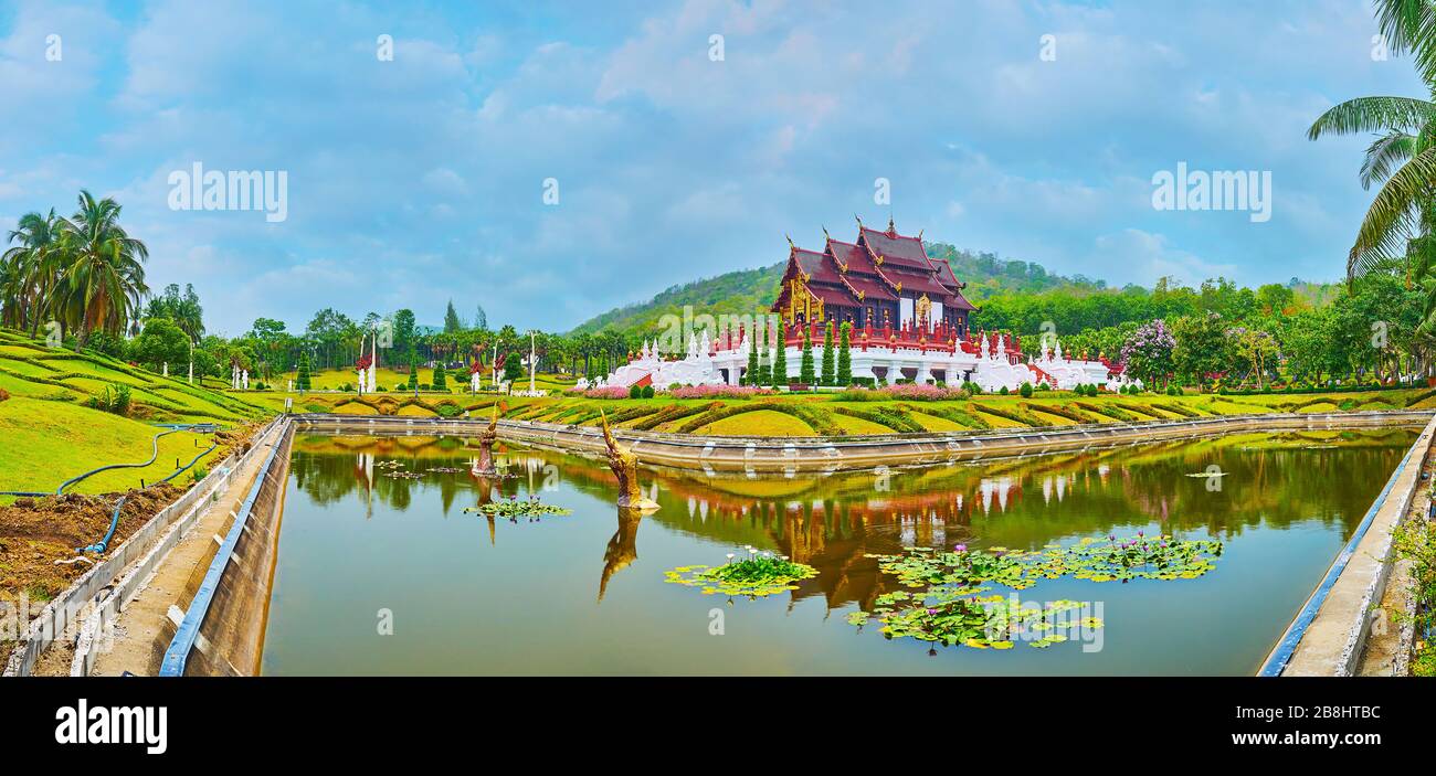 Panorama of impressive Royal pavilion with pyathat roof, surrounded by flower beds, juicy lawn and narrow canal, Rajapruek park, Chiang Mai, Thailand Stock Photo