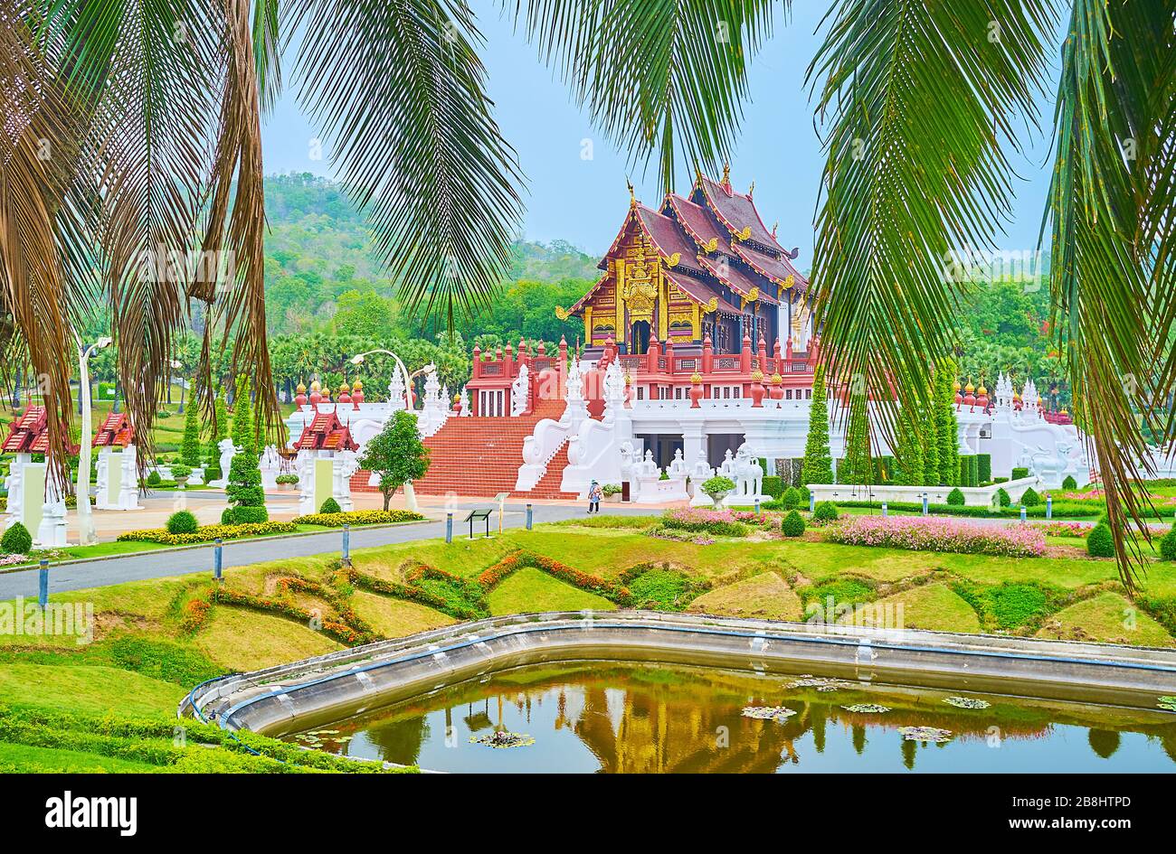 The view on magnificent Royal pavilion, surrounded by red staircases and white sculptures, through the lush green palm branches, Rajapruek park, Chian Stock Photo