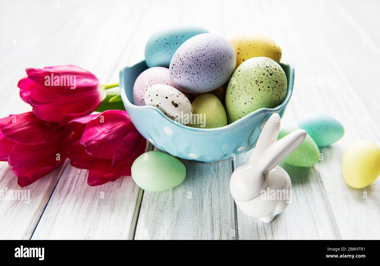 Easter background with colorful eggs in bowl and pink tulips on a white ...