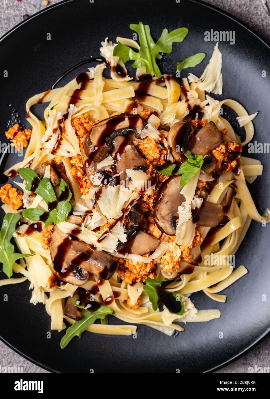 Bolognese pasta with mushrooms and arugula poured balsamic sauce. Top view. Macro. Stock Photo