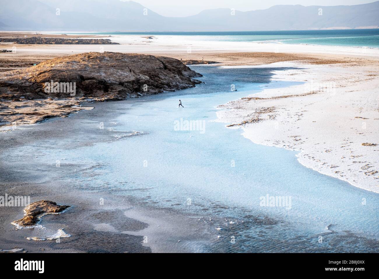 Africa, Djibouti, Lake Assal. Landscape view of lake Assal with people harvesting salt and a man crossing the water pound Stock Photo