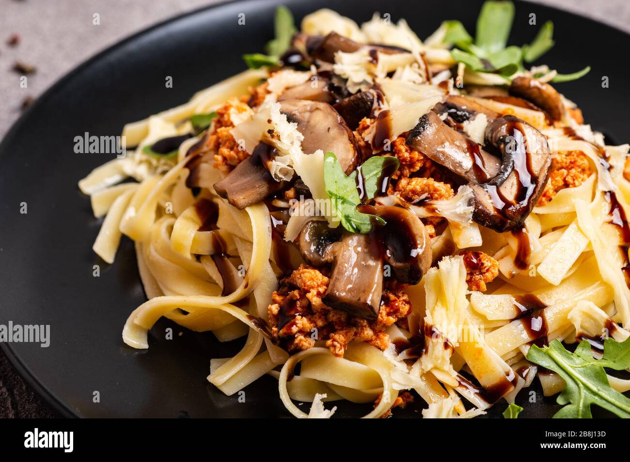 Bolognese pasta with mushrooms and arugula poured balsamic sauce on a black plate. Close-up. Stock Photo