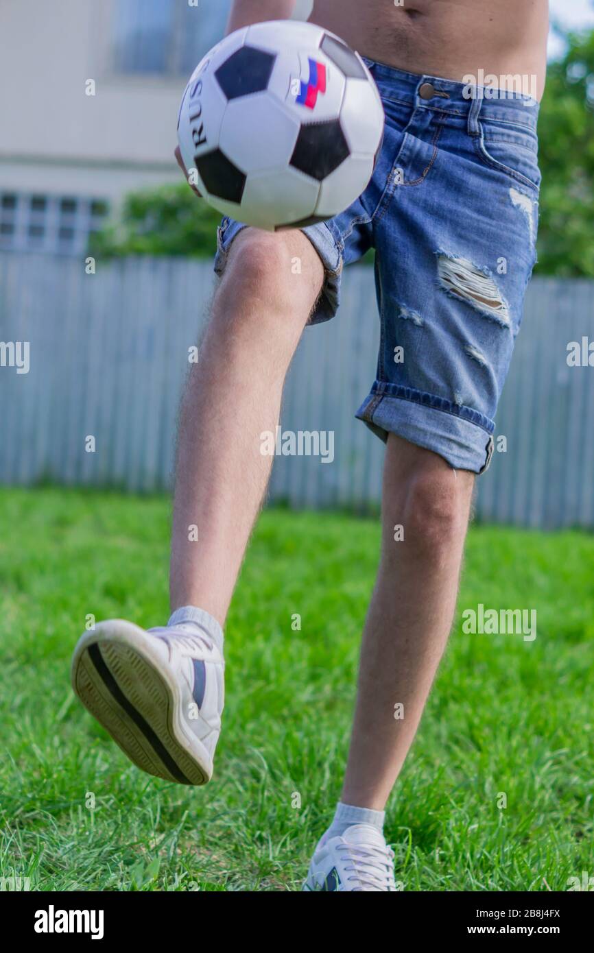 young man in denim jeans and white sneakers playing football ball
