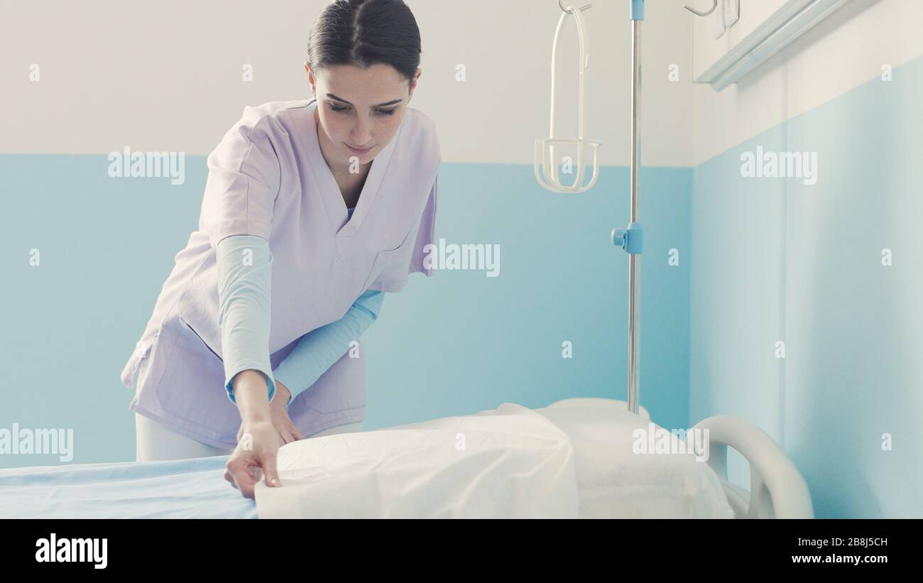 Young nurse working at the hospital, she is cleaning up the room and making the bed Stock Photo