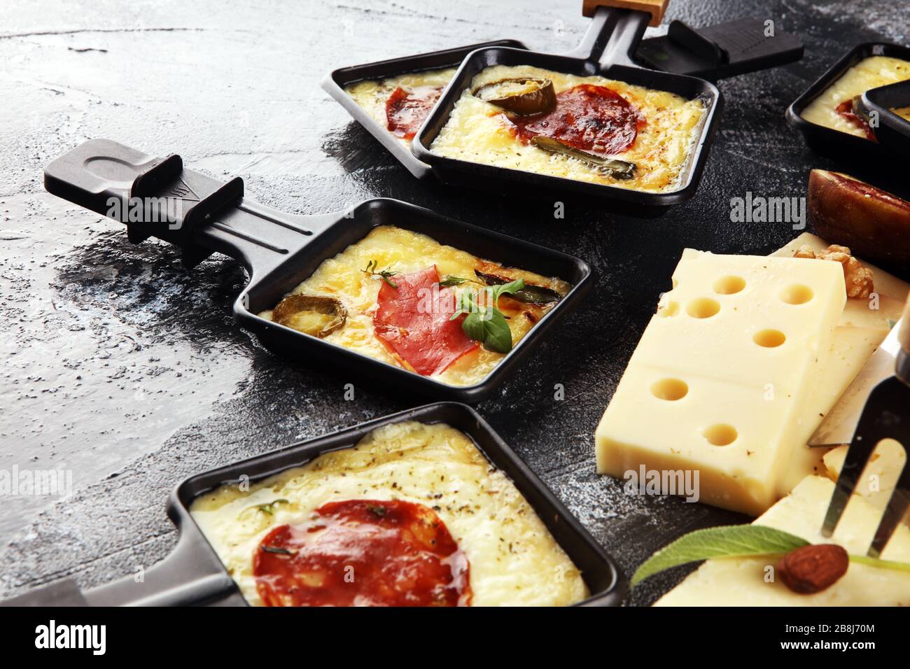 Delicious traditional Swiss melted raclette cheese on diced boiled or baked  potato served in individual skillets with salami and potatoes Stock Photo -  Alamy