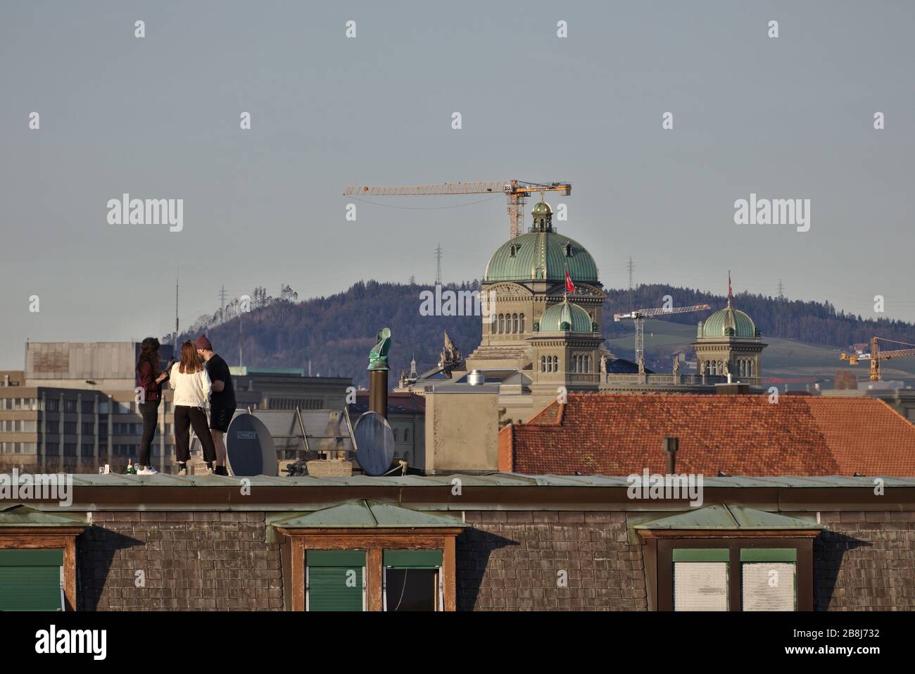 Bern, Switzerland, March 2020: Federal Council ordering people to stay home due to Coronavirus pandemic. Young adults on roof in front of parliament. Stock Photo
