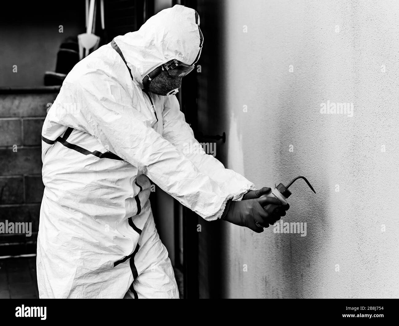 Healthcare worker with full white coverall disinfects from possible infection with Coronavirus Covid-19, using a hydro alcoholic spray solution Stock Photo