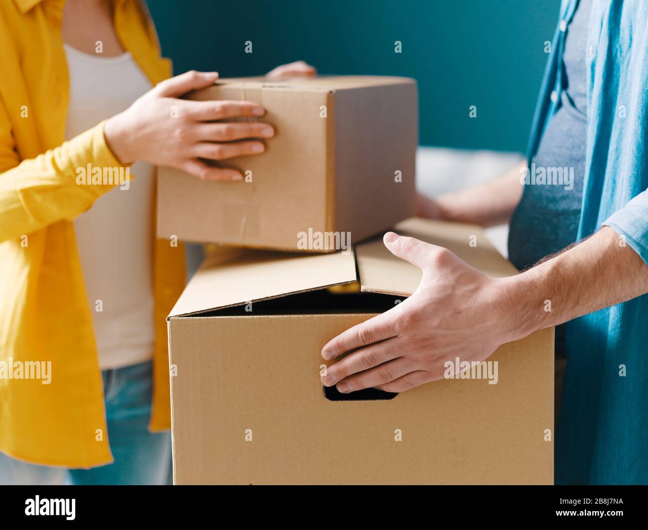 Happy couple moving in their new house: the man is carrying a box and ...