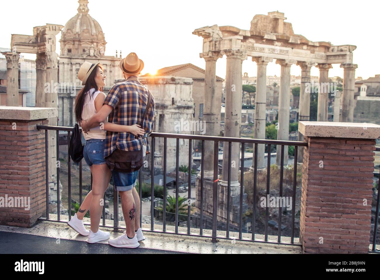 Young couple tourist looking at Roman Forum at sunrise hugging. Historical imperial Foro Romano in Rome, Italy from panoramic point of view. Stock Photo