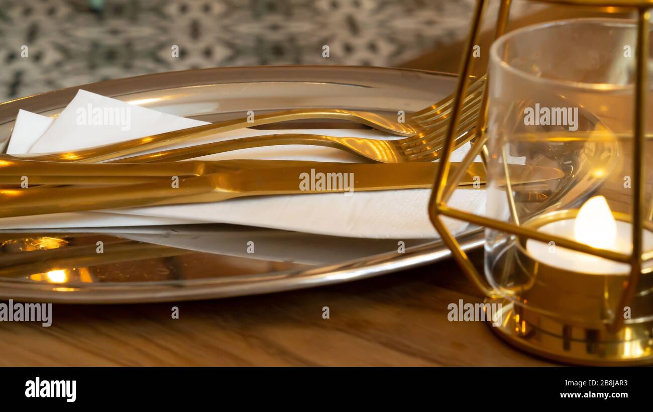 Gold cutlery on a silver tray ready for serving some food at breakfast, lunch or dinner next to a golden lamp Stock Photo