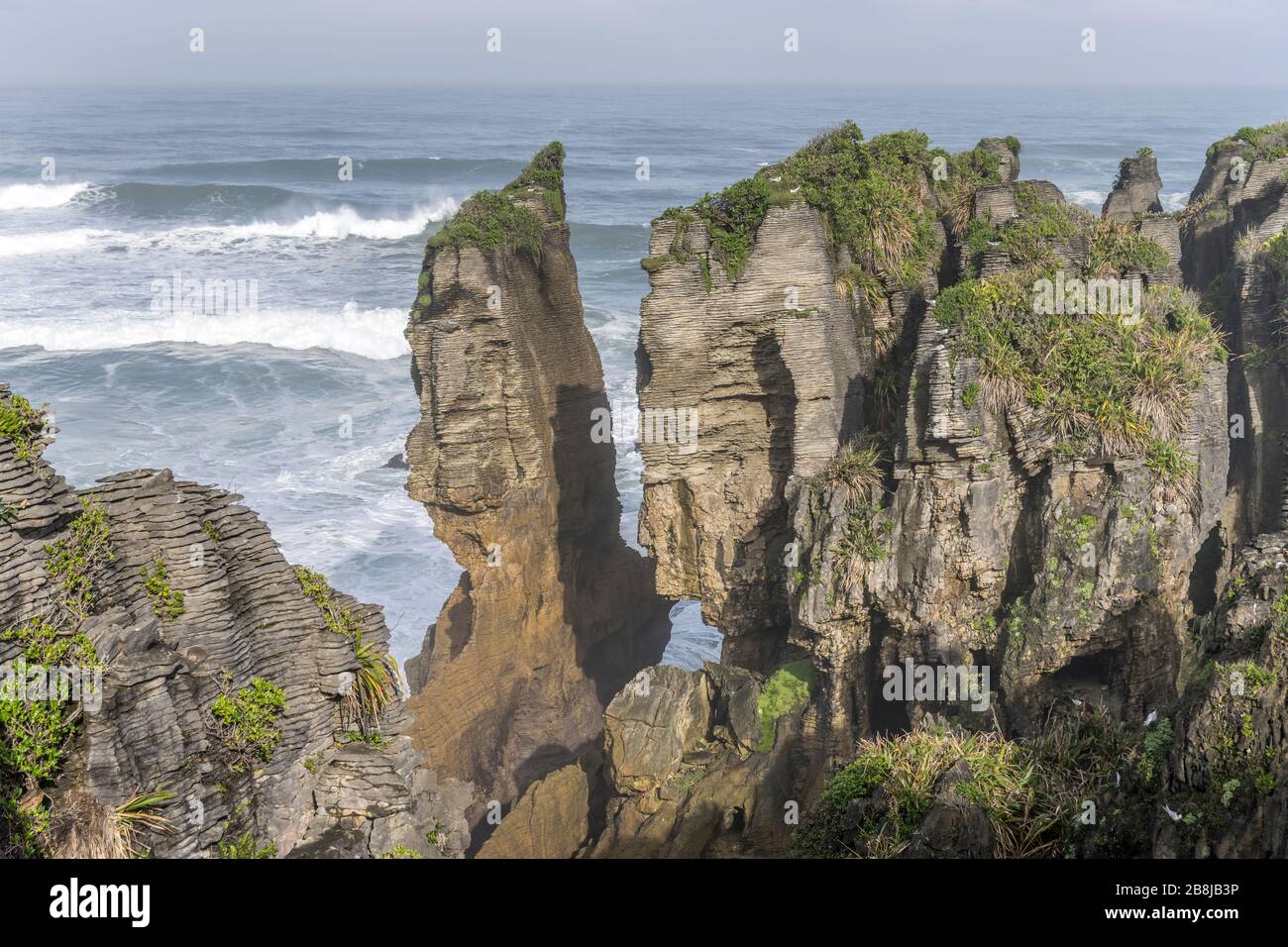 platy rocks of worn cliffs and Tasman sea waves at shore, shot in bright spring light at Punakaiki, West Coast, South Island, New Zealand Stock Photo