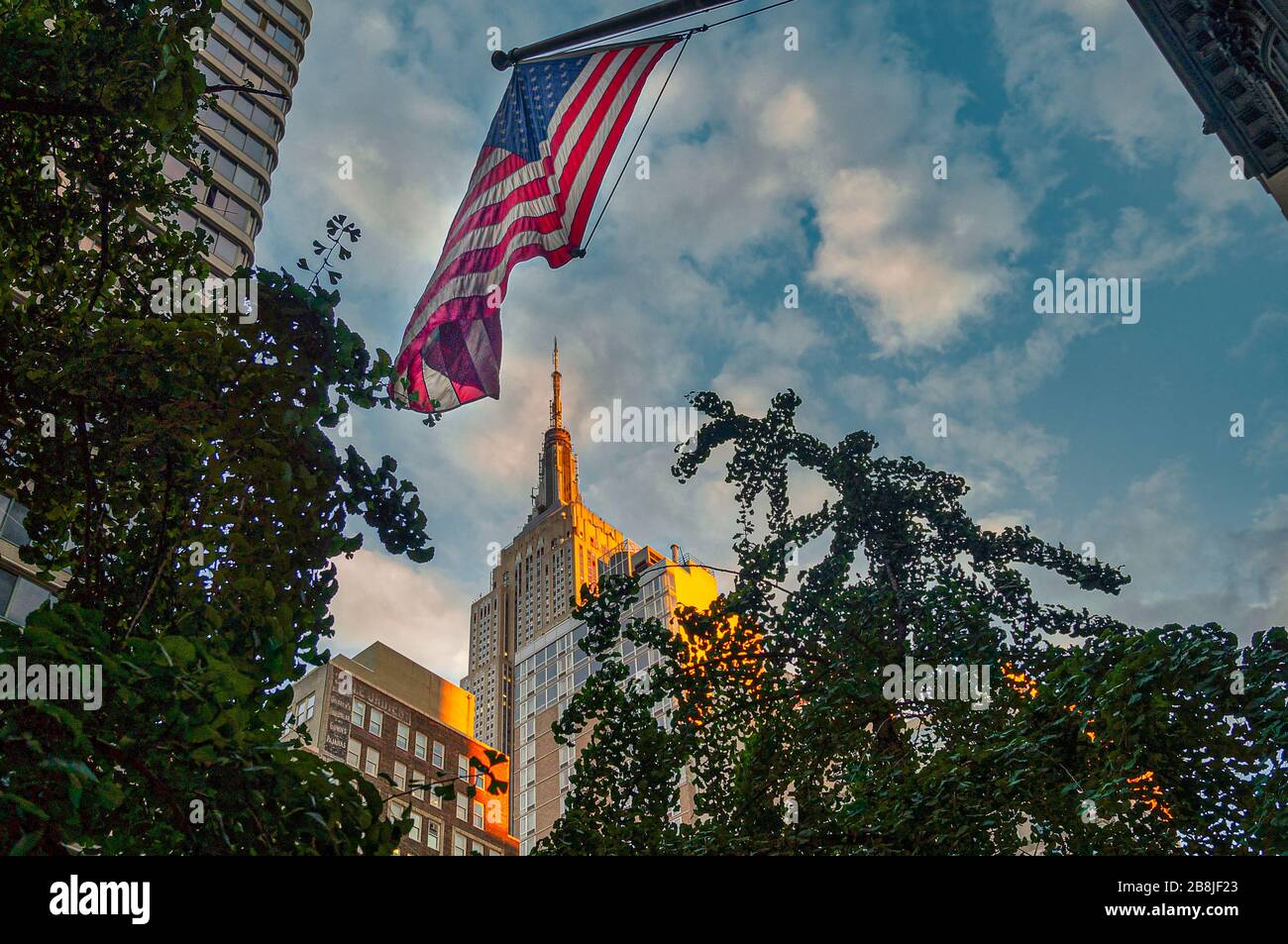 Low perspective view to the illuminated Empire State Building in New York and the hanging USA star spangled banner flag. Stock Photo