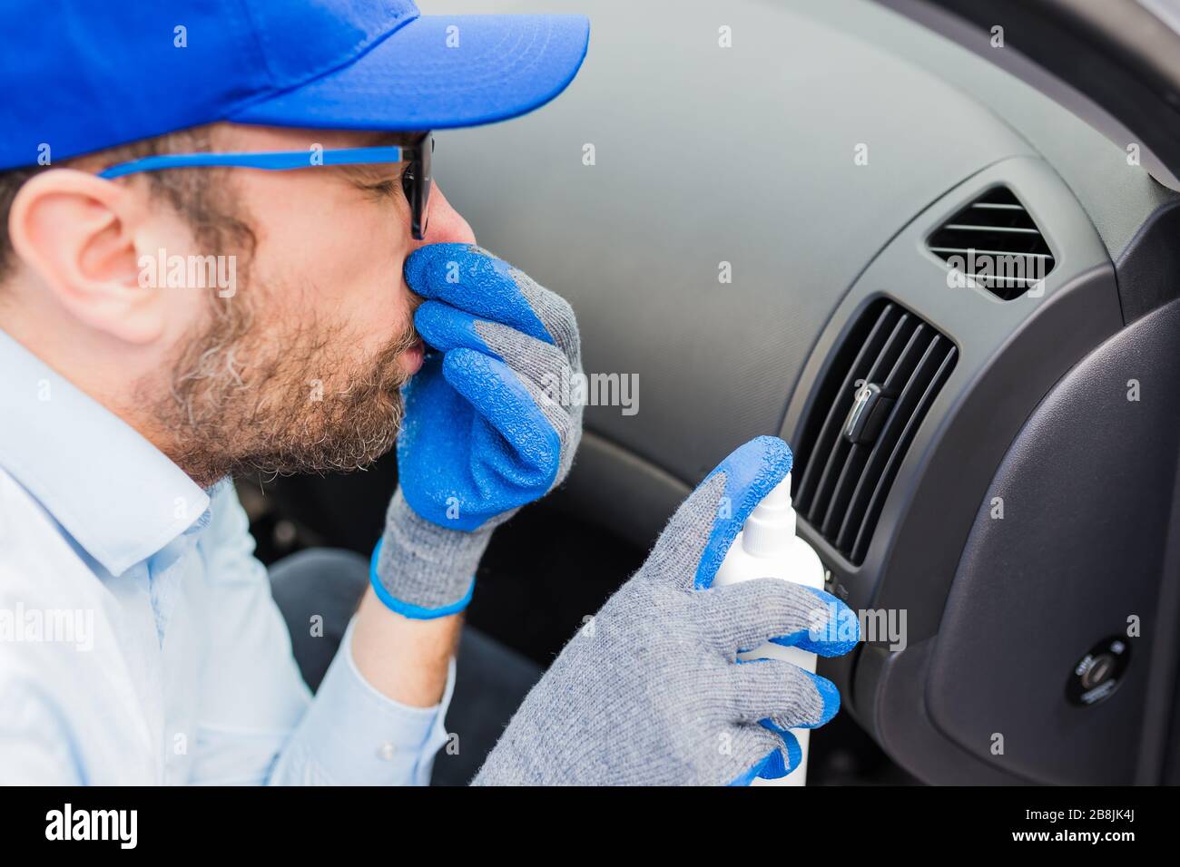Car wash employee covering his nose with hand and using bottle with