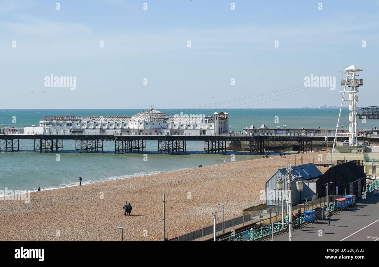 Brighton UK 22nd March 2020 - Visitors enjoy some Spring sunshine today on Brighton beach which looks quiet this lunchtime during the Coronavirus COVID-19 pandemic crisis . Credit: Simon Dack / Alamy Live News Stock Photo