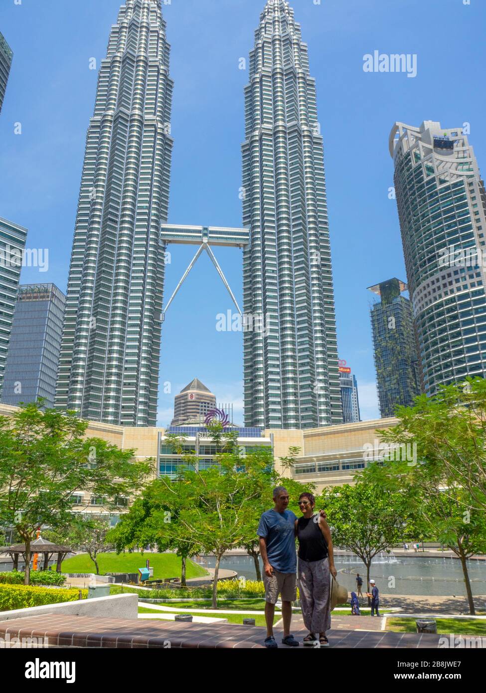 Tourist couple standing in KLCC Park in front of the Petronas Twin Towers and Suria KLCC Shopping Mall Kuala Lumpur Malaysia. Stock Photo
