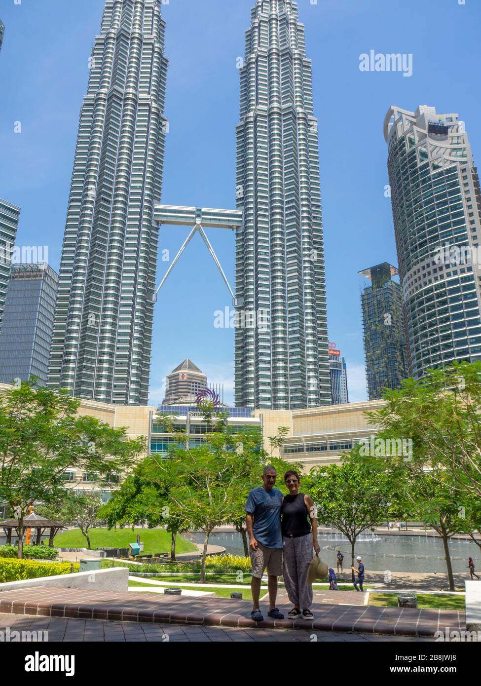 Tourist couple standing in KLCC Park in front of the Petronas Twin Towers and Suria KLCC Shopping Mall Kuala Lumpur Malaysia. Stock Photo