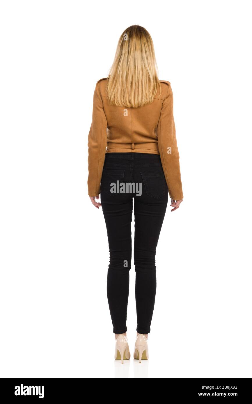 Rear view of standing young woman in brown suede leather jacket, black jeans and high heels. Full length studio shot isolated on white. Stock Photo