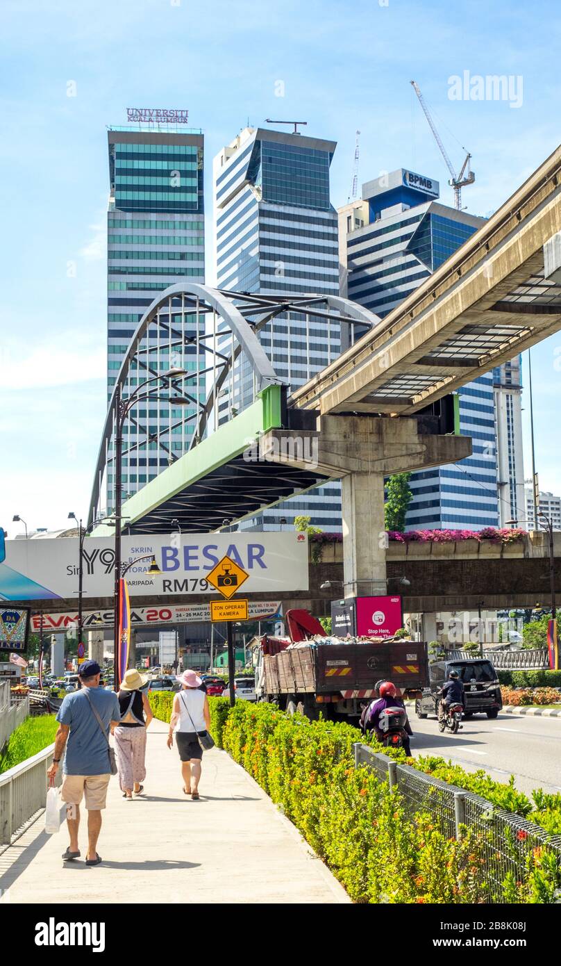 Tourists walking on footpath along Jalan Sultan Ismail, overhead KL Monorail Line and office towers in Kuala Lumpur Malaysia. Stock Photo