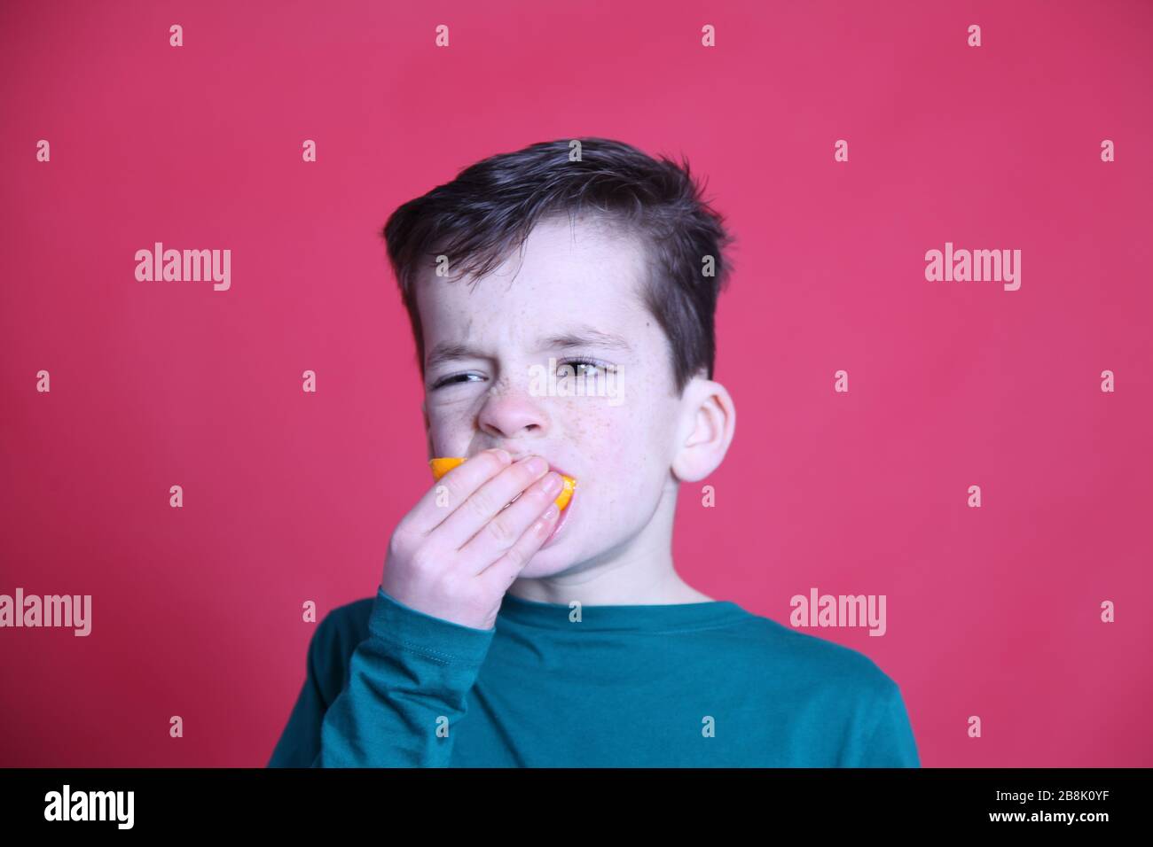 UK 8 year old boy eating orange fruit slice, red background, UK 2020