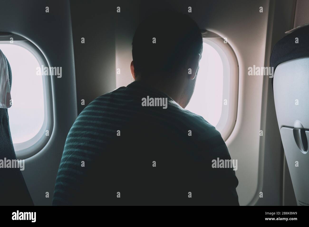 A back view of a man seated on an airplane, watching the view from the plane window. Stock Photo
