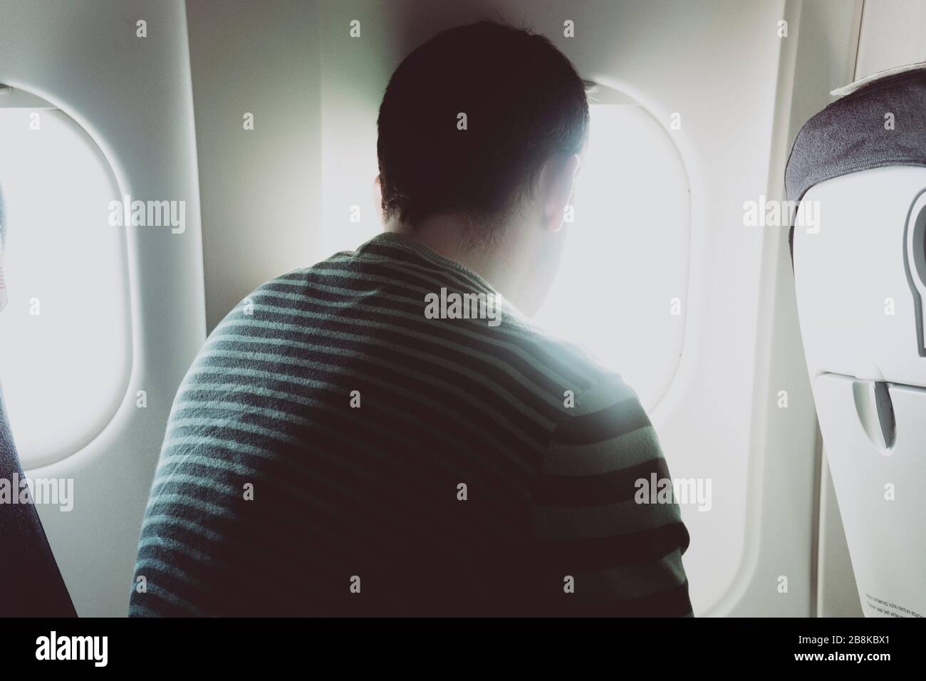 A back view of a man seated on an airplane, watching the view from the plane window. Stock Photo