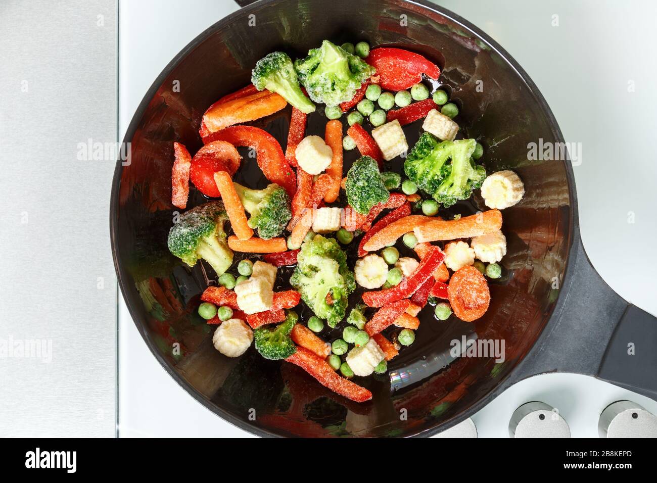 Frying frozen mix vegetables in a pan. Prefabricated top view close-up. Stock Photo