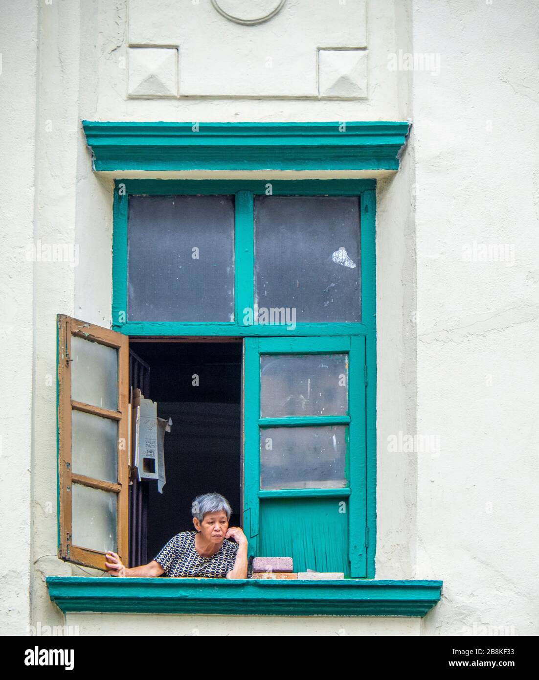 Elderly woman sitting at her shophouse apartment window looking at the street below, Jalan Tuanku Abdul Rahman Kuala Lumpur Malaysia. Stock Photo