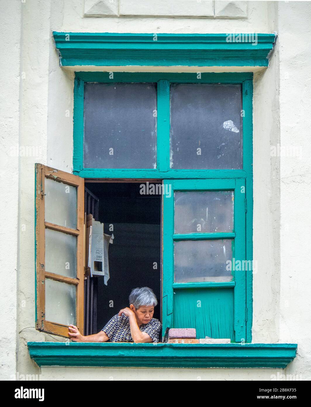 Elderly woman sitting at her shophouse apartment window looking at the street below, Jalan Tuanku Abdul Rahman Kuala Lumpur Malaysia. Stock Photo