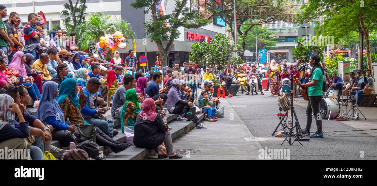 Man playing guitar free concert  street performance if front of audience in tree lined Jalan Tuanku Abdul Rahman street central Kuala Lumpur Malaysia. Stock Photo