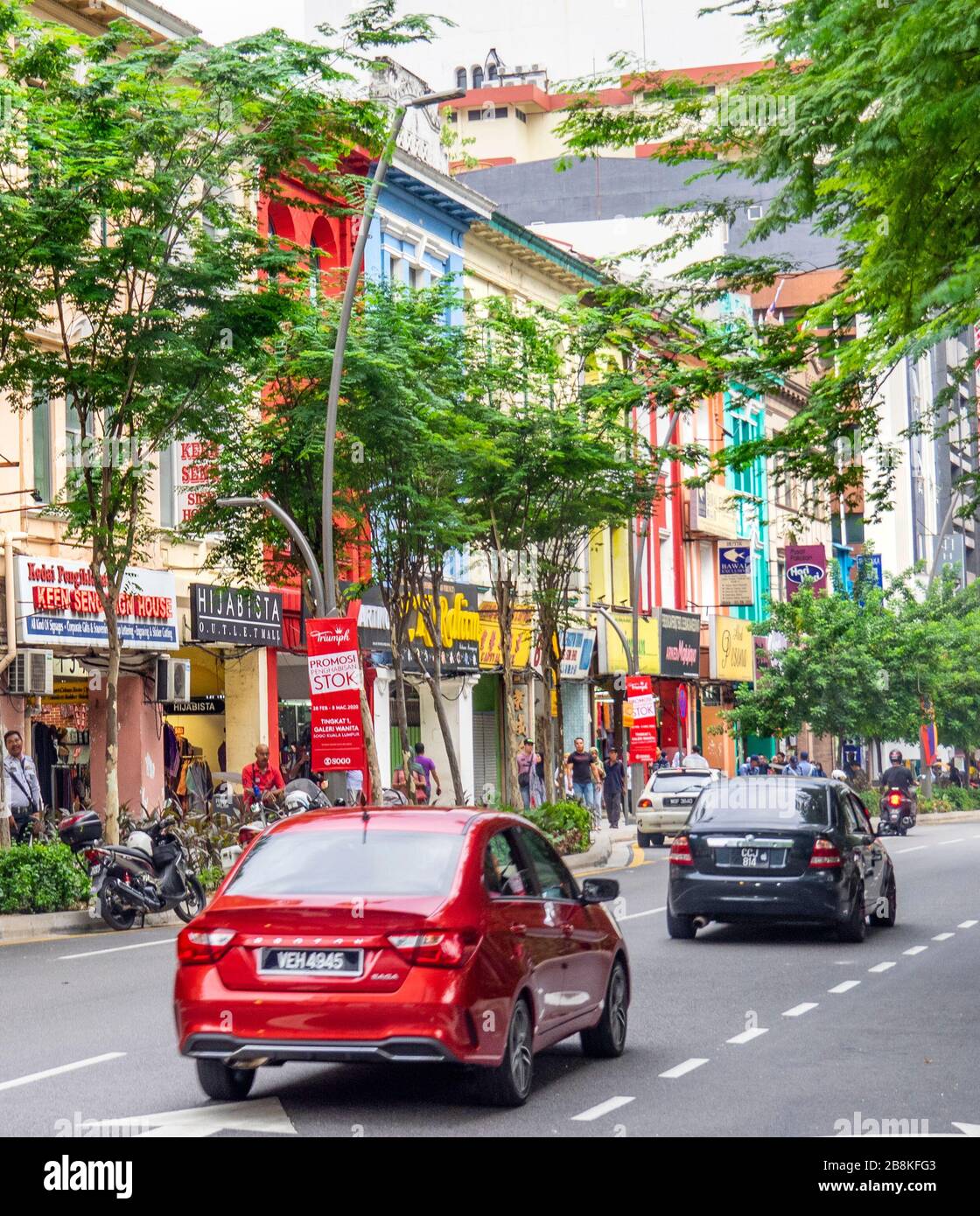 Traffic in tree lined street Jalan Tuanku Abdul Rahman and terrace shophouses with fabric and textile shops Kuala Lumpur Malaysia Stock Photo
