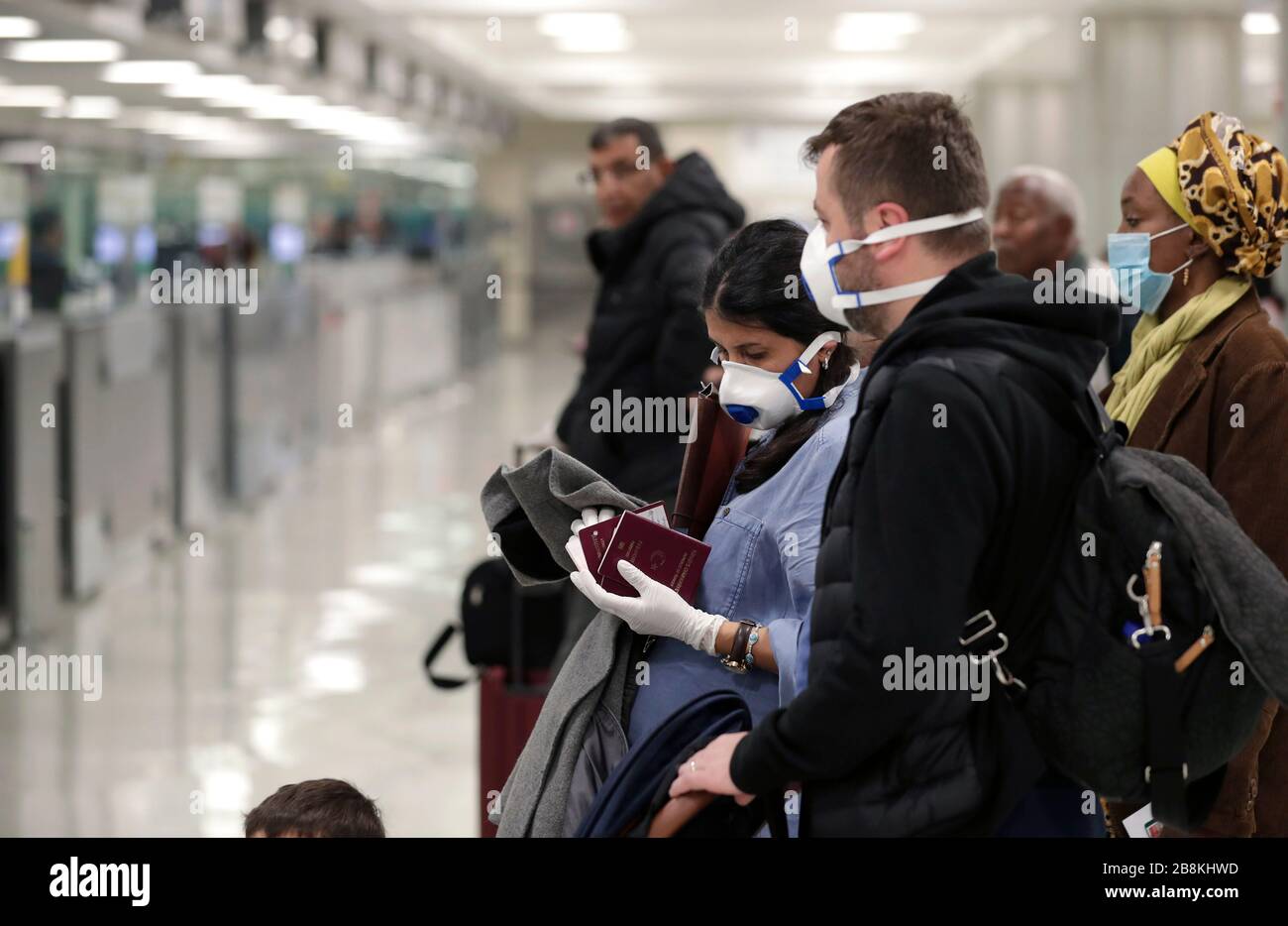 Passengers arriving at Dulles International Airport wearing personal protective equipment March 13, 2020 in Dulles, Virginia. In response to the COVID-19, coronavirus pandemic CBP officers and travelers have begun wearing gloves and masks as protection from viral exposure. Stock Photo