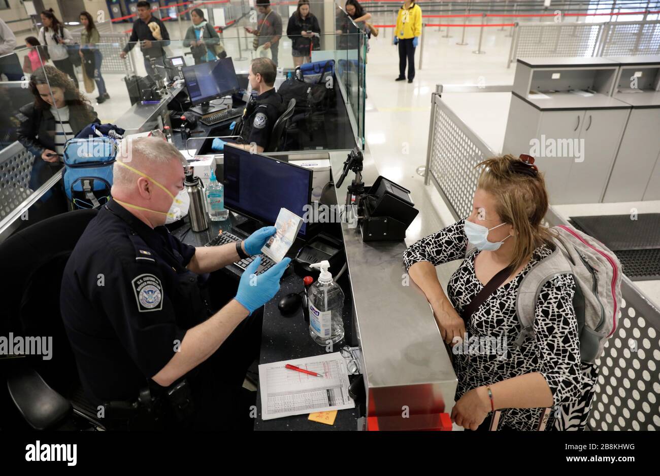 U.S. Customs and Border Protection officers screen international passengers arriving at Dulles International Airport wearing personal protective equipment March 13, 2020 in Dulles, Virginia. In response to the COVID-19, coronavirus pandemic CBP officers and travelers have begun wearing gloves and masks as protection from viral exposure. Stock Photo