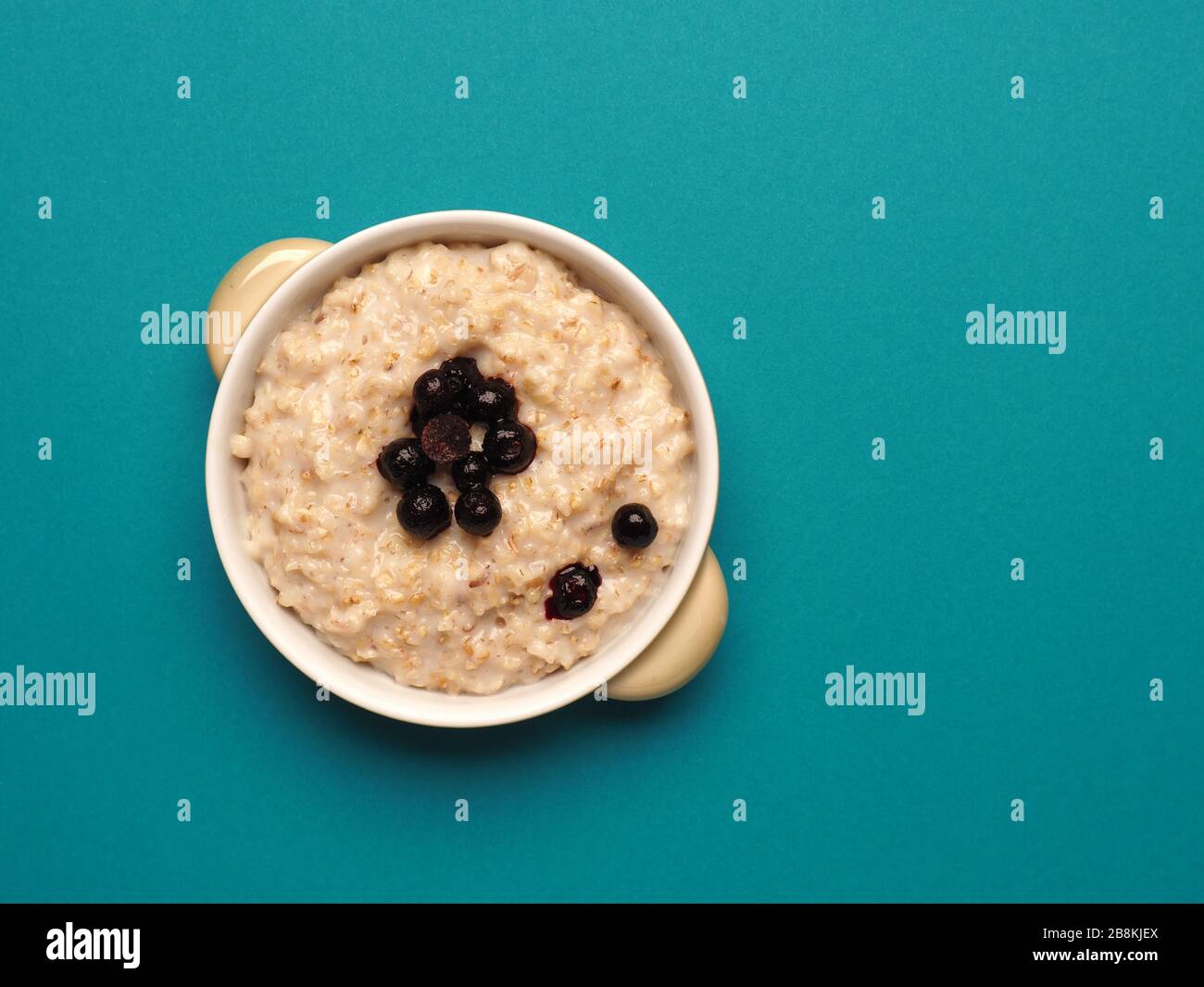 Hot porridge with frozen blueberries on a turquoise background with space for text, view from