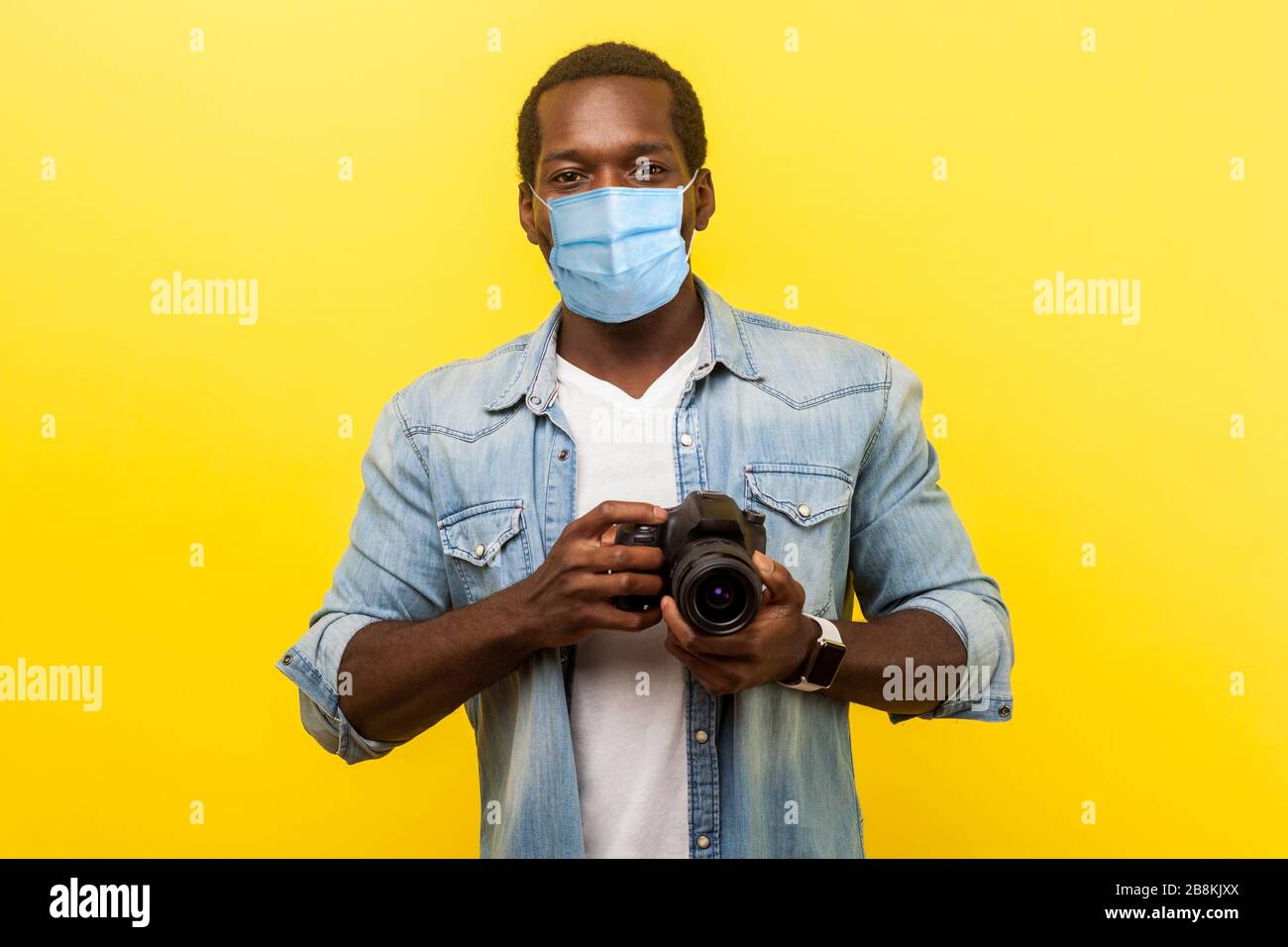 Portrait of positive photographer, man with medical mask holding professional digital dslr camera and looking with toothy smile, enjoying his job. ind Stock Photo