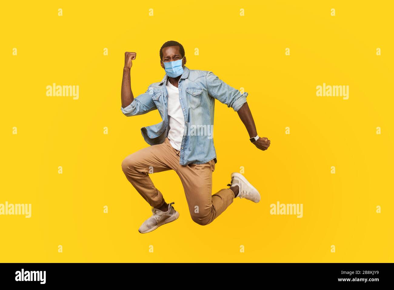 Full length portrait of joyous ecstatic man with medical mask jumping for joy or flying with raised hand, gesturing yes i did it, celebrating success. Stock Photo