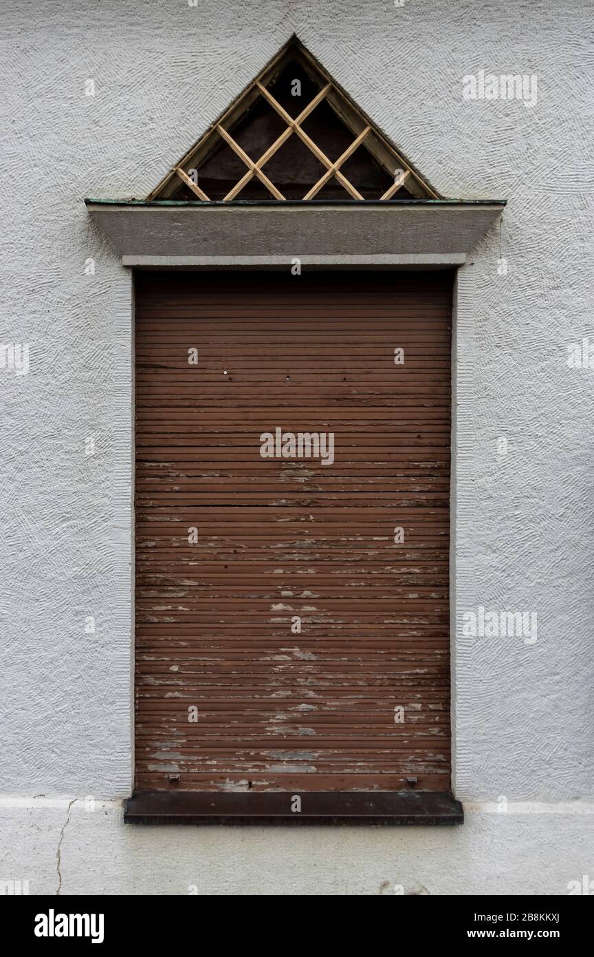 Facade with high windows and closed old wooden shutters, triangular skylight with grille as burglar protection and plaster in spatula technique Stock Photo