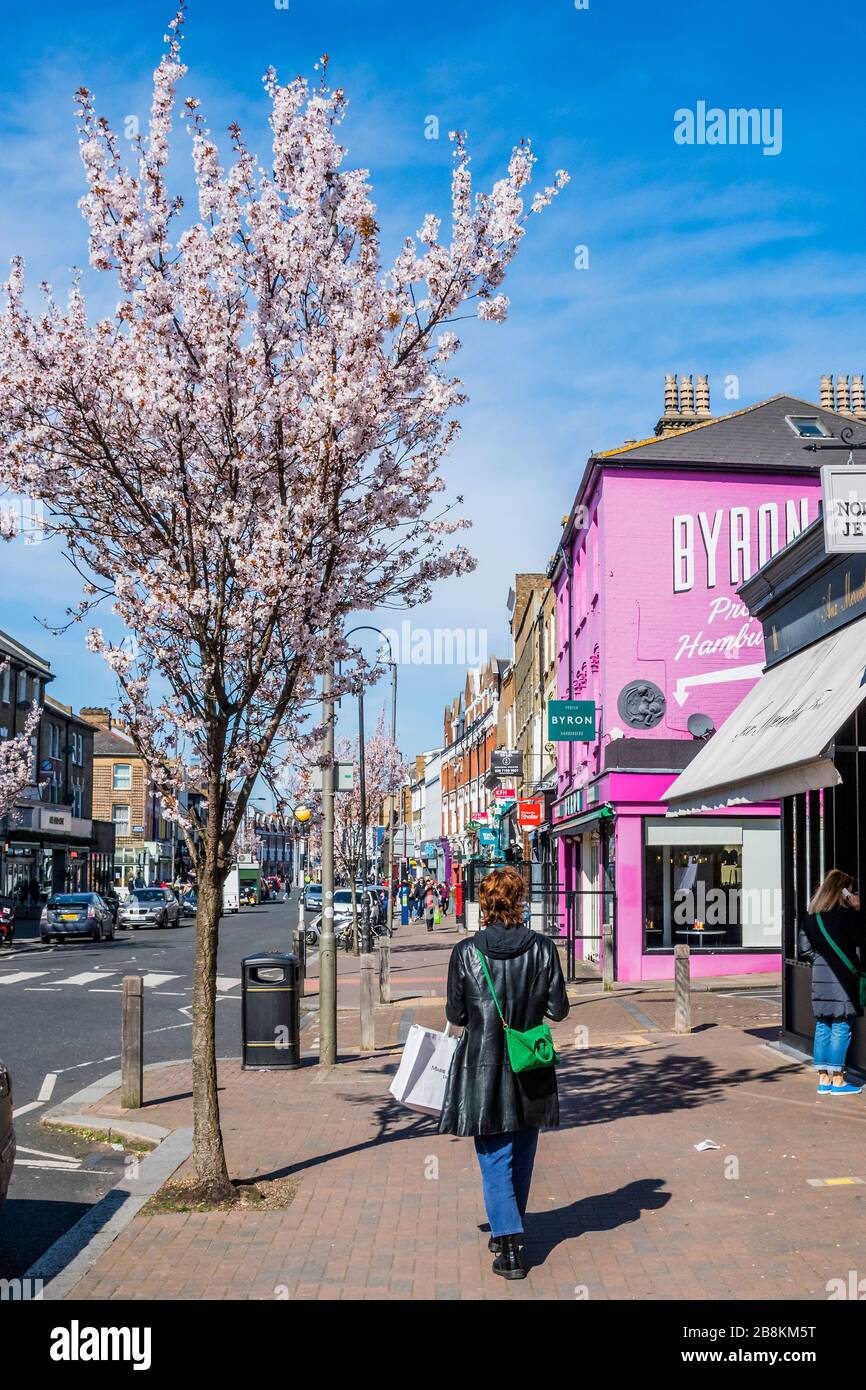 London, UK. 22nd Mar 2020. Life goes on for Mother's Day, under blue skies and with the tree blossom out, on Northcote Road. However the normally busy restaurants are now all closed - Anti Coronavirus (Covid 19) outbreak in London. Credit: Guy Bell/Alamy Live News Stock Photo