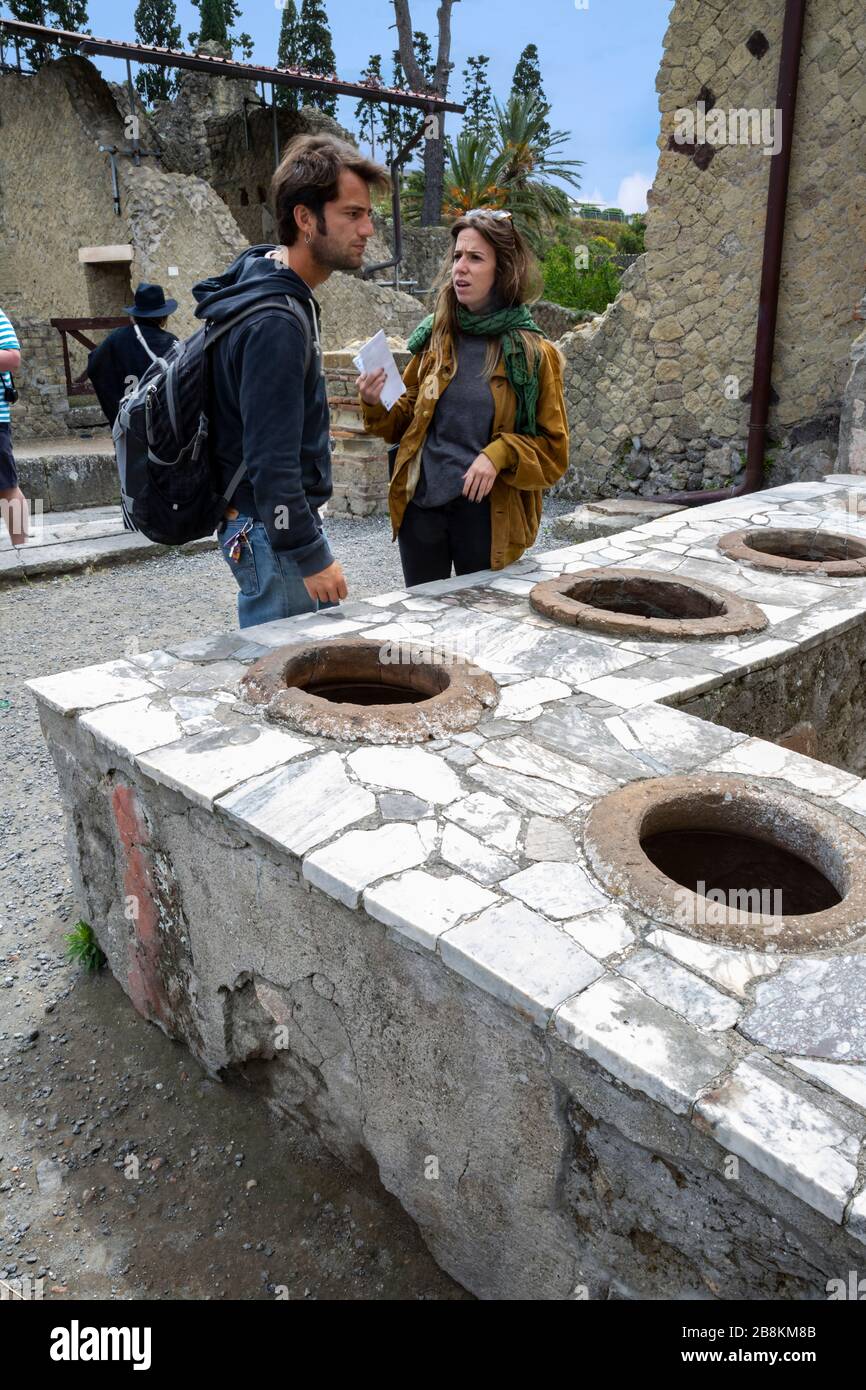 Tourists exploring the ruins of an ancient fast food shop, Herculaneum, Campania, Italy. Stock Photo