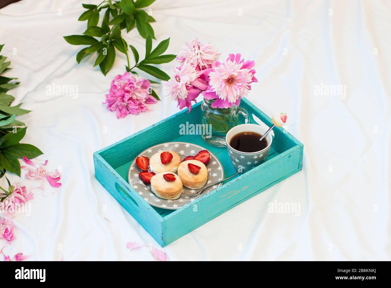 Breakfast in bed with cottage cheese pancakes, fresh strawberries, peonies and cup of coffee. White background. Stock Photo