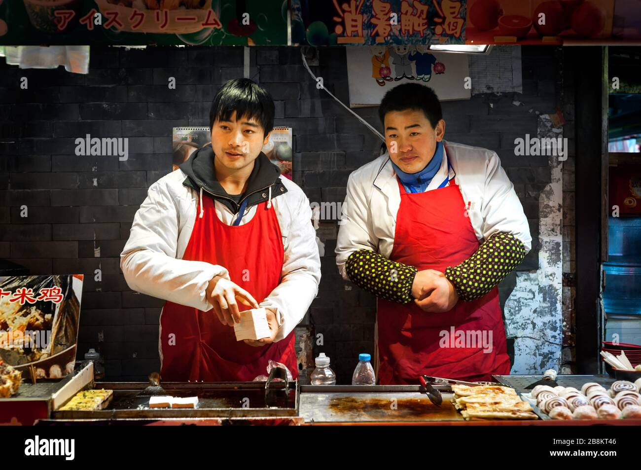 WANGFUJING NIGHT MARKET, BEIJING - DEC 25, 2013 - Two young snack vendors at Wangfujing snack street, Beijing Stock Photo