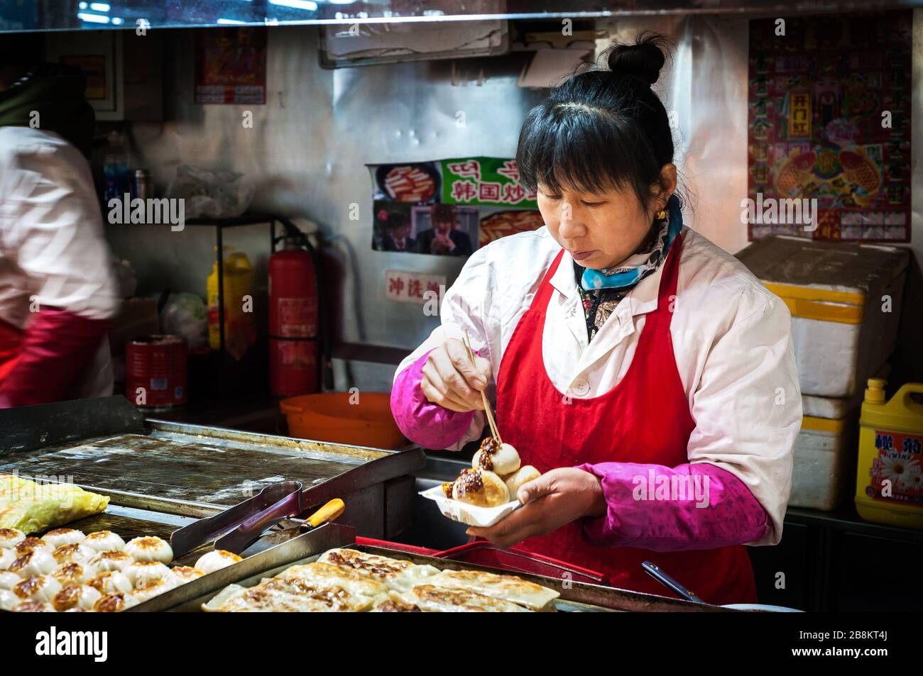 WANGFUJING NIGHT MARKET, BEIJING - DEC 25, 2013 - Female vendor serving fried pork buns at Wangfujing snack street, Beijing Stock Photo