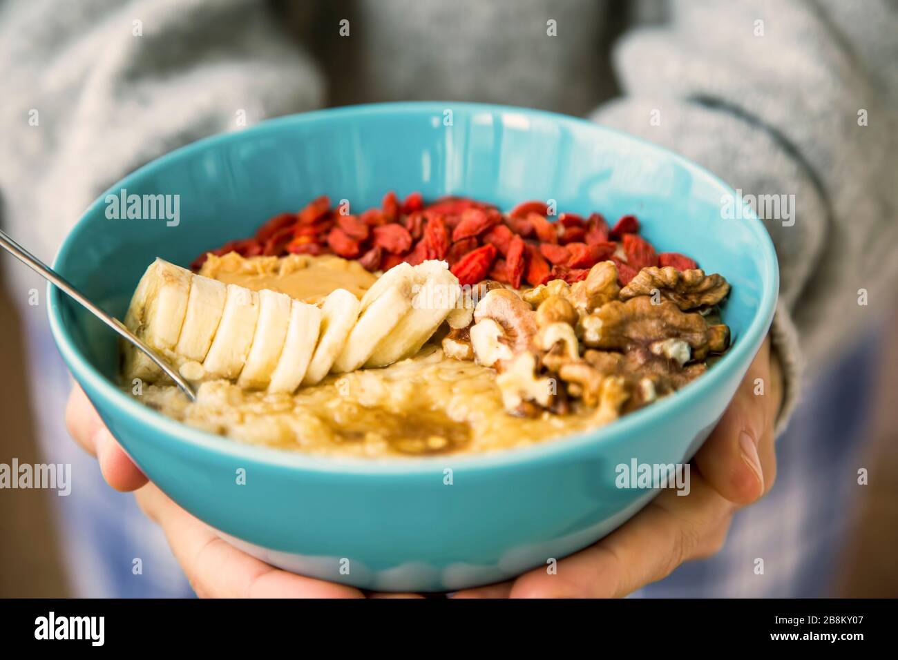 Porridge bowl in woman hands, front view of cozy warm winter healthy oatmeal with goji fruits and nuts Stock Photo