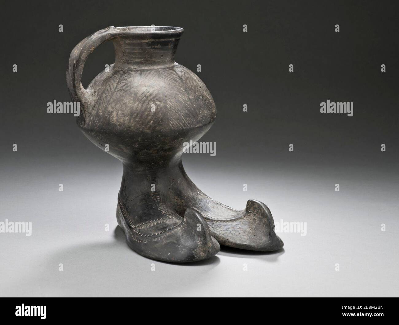 'Handled Jar with Boots (image 1 of 2); Furnishings; Serviceware Black burnished ware Height:  6 1/2 in. (16.8 cm); Width:  6 1/2 in. (16.7 cm); Diameter:  4 1/2 in. (11.3 cm) Gift of Nasli M. Heeramaneck (M.76.174.179) Art of the Ancient Near East Currently on public view:; between circa 1350 and circa 800 B.C.; ' Stock Photo